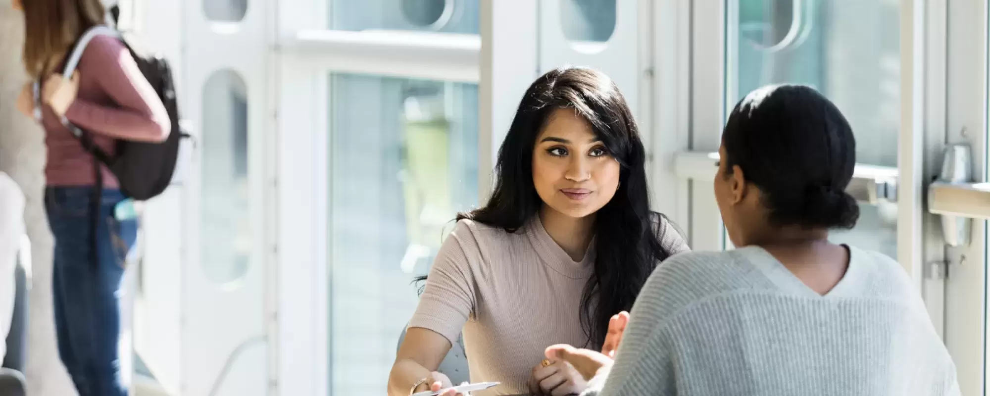 Two young women sitting at a table talking to each other