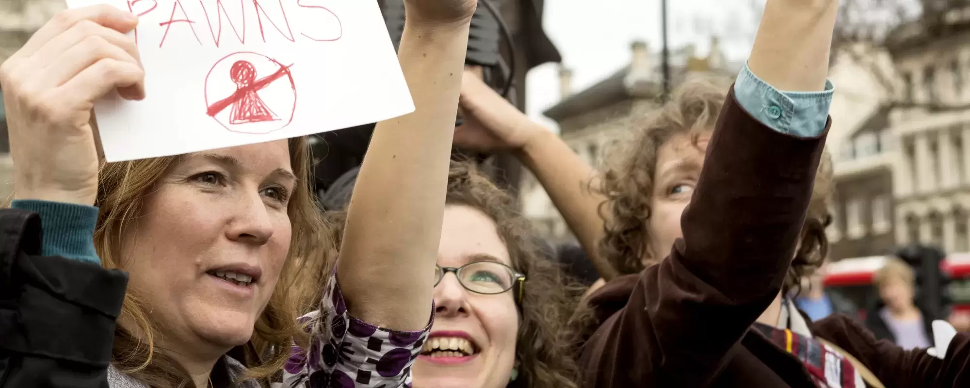 People at march holding up flags and a sign saying "People not pawns"