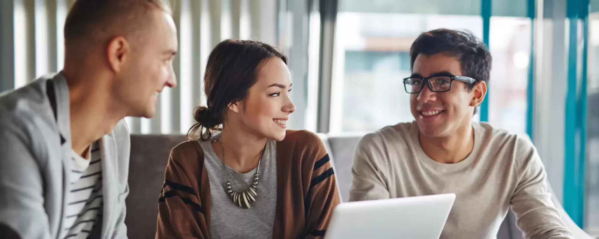 Three people talking smiling in front of a laptop