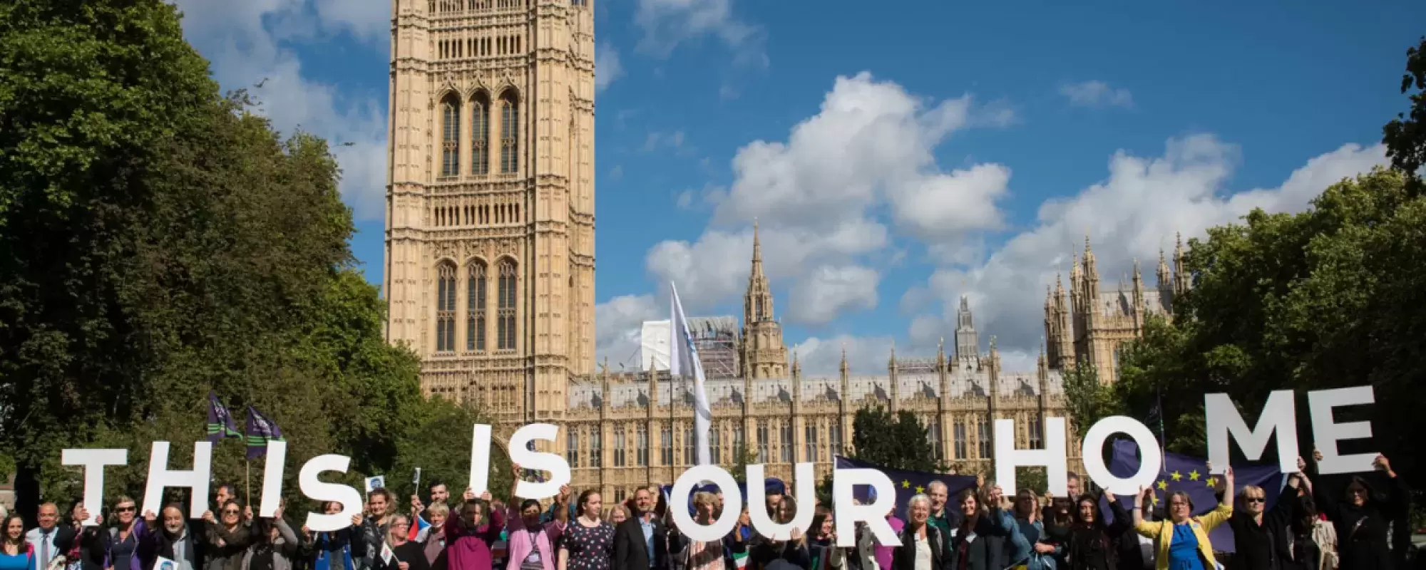 A group of people in front of Houses of Parliament holding up big letters saying "This is our home"
