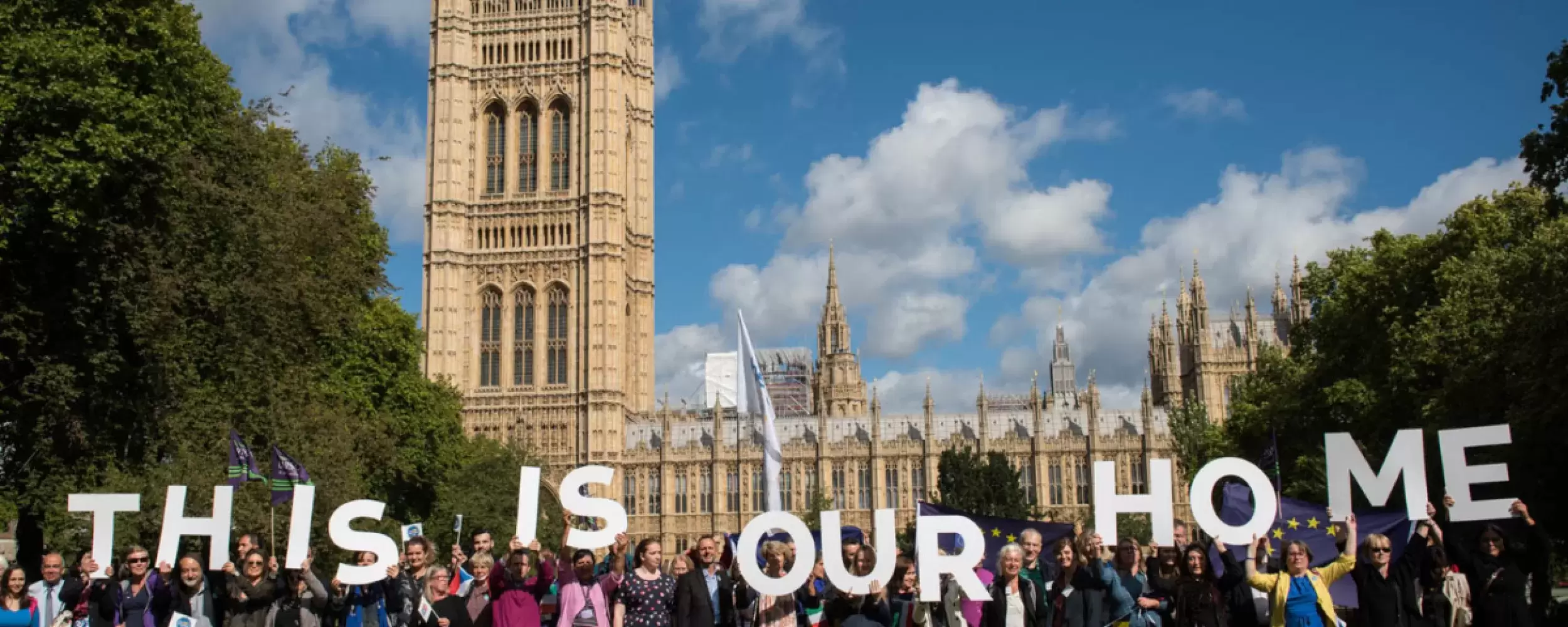 A group of people in front of Houses of Parliament holding up big letters saying "This is our home"